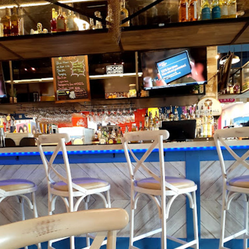 A vibrant bar area with white stools, a blue-lit counter, and shelves of liquor bottles.