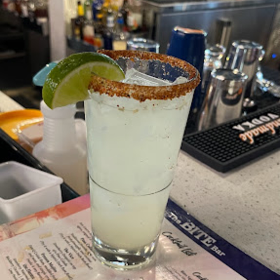 A margarita with a chili-lime rim and a lime wedge sits on a bar next to a menu.