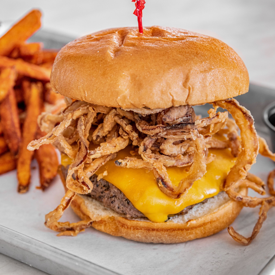 A Bite Eatery cheeseburger with crispy fried onions and sweet potato fries on a metal tray.