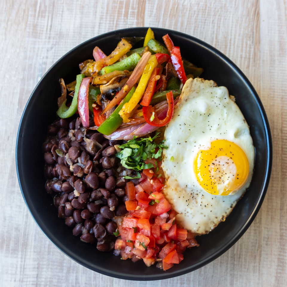 A breakfast bowl with black beans, bell peppers, diced tomatoes, cilantro, and a fried egg.